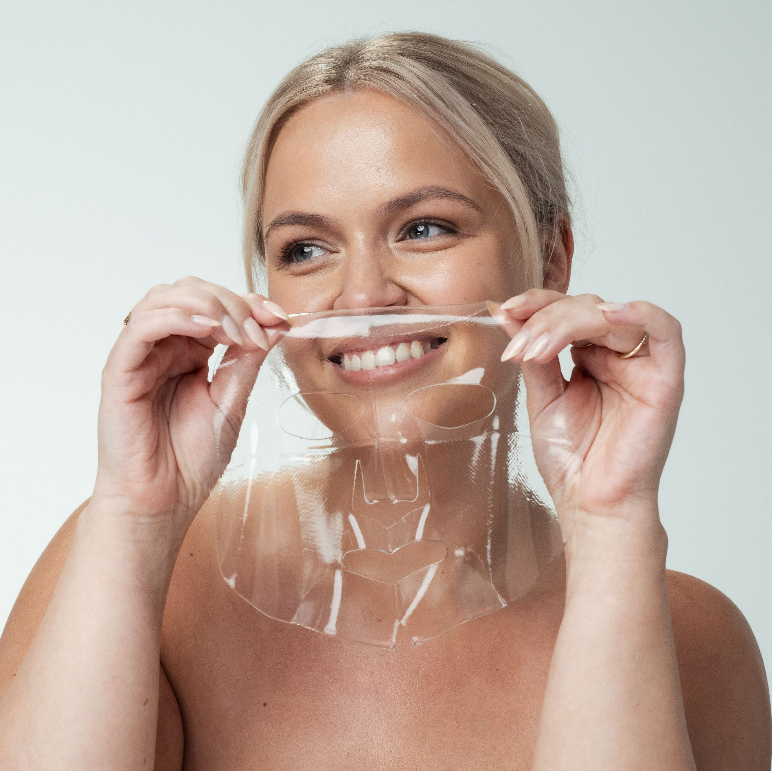 Woman holding a clear face mask against a plain background