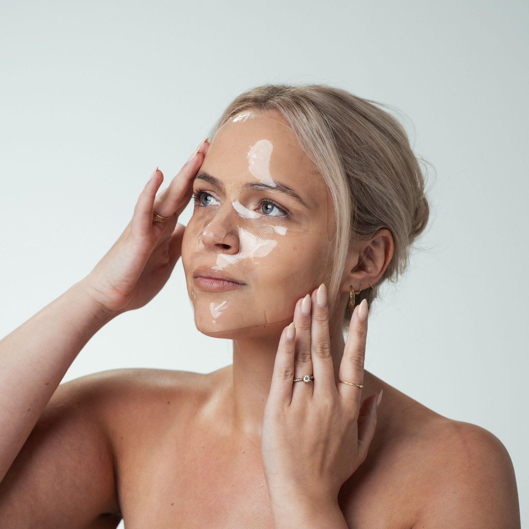Woman applying a sheet mask to her face with a neutral background